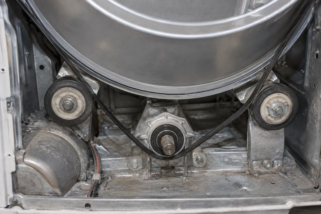 The open rear of an electric clothes dryer showing the drum support rollers, belt and bearing clustered at the base of the drum.