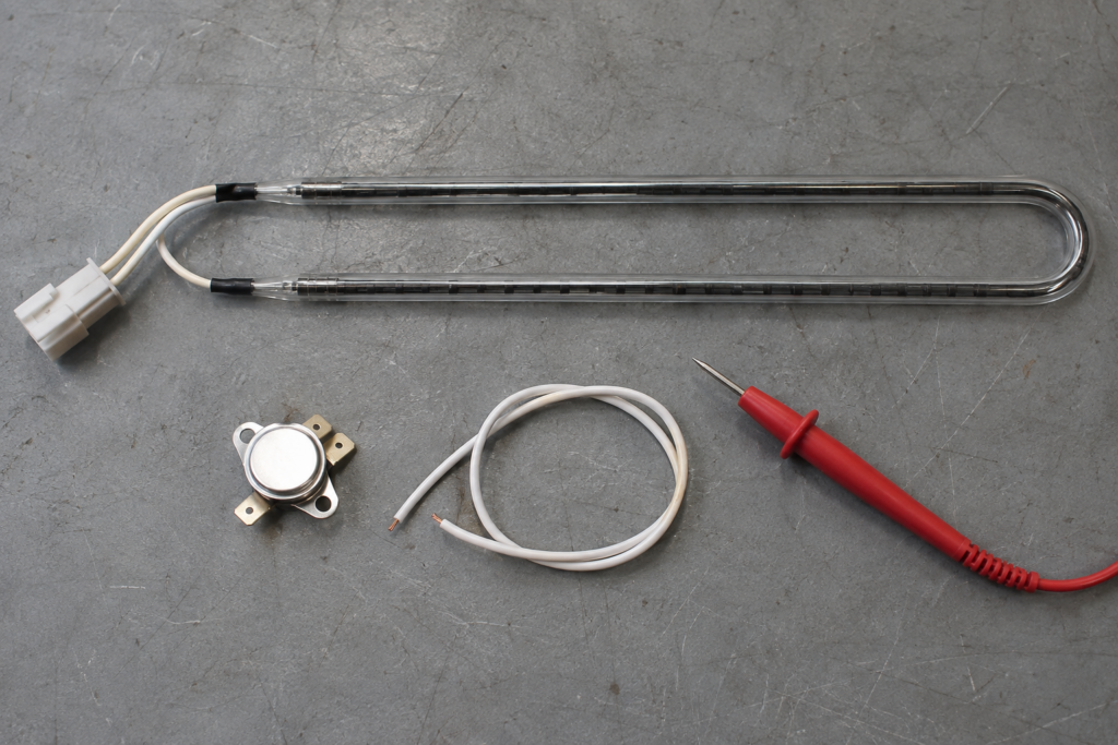 A defrost heater, a bi-metal thermostat and a wire lead laid out on a grey workbench mat.